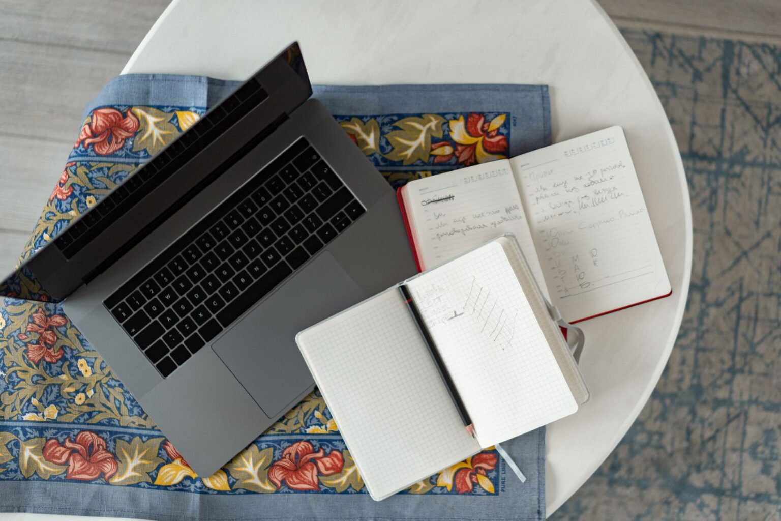 Person writing notes at a desk with a laptop open, representing content creation workflow
