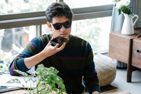 A person recording a voice memo on a smartphone at a desk with a notebook nearby
