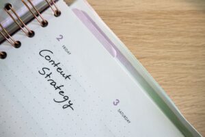 A content calendar spread open on a desk next to a laptop showing social media scheduling