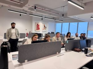 Marketing team members collaborating around a shared digital workspace on laptops
